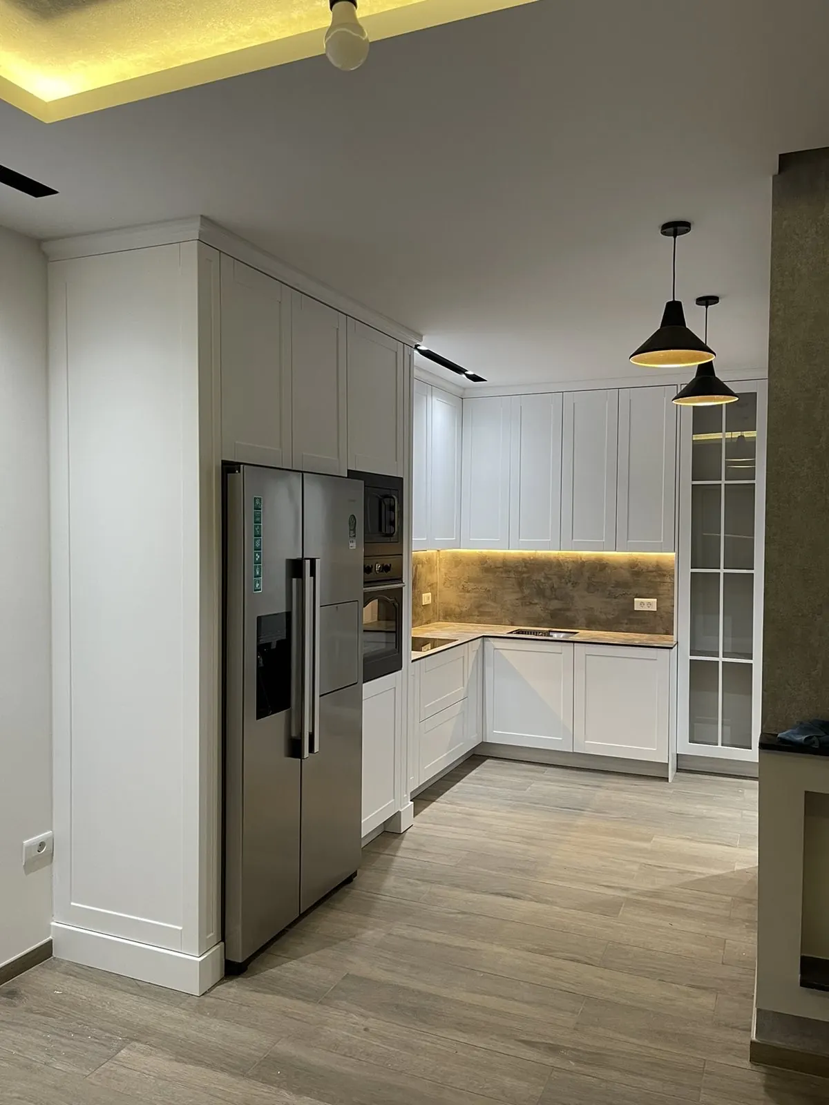 Weiße Küche mit Hochschränken, Side-by-Side-Kühlschrank und beleuchteter Arbeitsfläche
